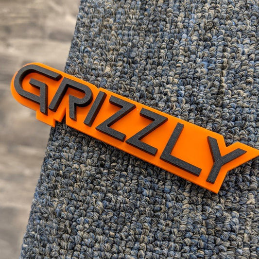 Badge de voiture Grizzly - Noir mat sur orange - Police Squid - Montage sur ruban adhésif